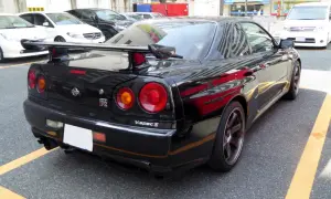Czarny Nissan GT-R R34 V-spec II z charakterystycznymi okrągłymi światłami i dużym spojlerem, zaparkowany na ulicy.