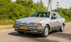 Srebrny Ford Scorpio z lat 90. pędzi po wiejskiej drodze, otoczony zielenią.