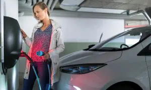 Kobieta podłącza kabel do ładowania samochodu elektrycznego w garażu podziemnym bloku.