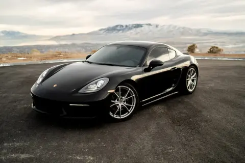 Czarny Porsche Cayman na tle gór i jeziora. Zastanawiasz się, ile kosztuje Porsche?