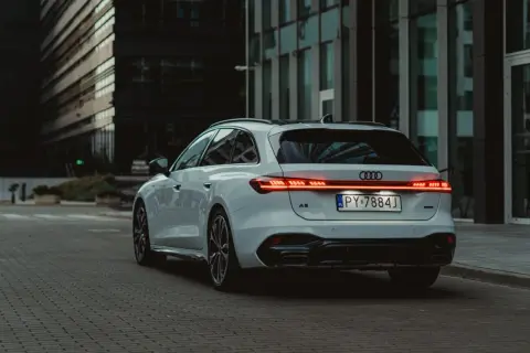 Białe Audi A5 Avant 2025 z nowoczesnym pasem świateł LED na klapie bagażnika, zaparkowane na tle szklanych budynków.