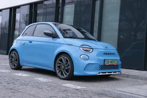 Niebieski Abarth 500e, gotowy do testu, zaparkowany przed nowoczesnym budynkiem.