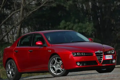 Czerwone Alfa Romeo 159 1.9 JTD z charakterystycznym grillem, zaparkowane na tle drzew.