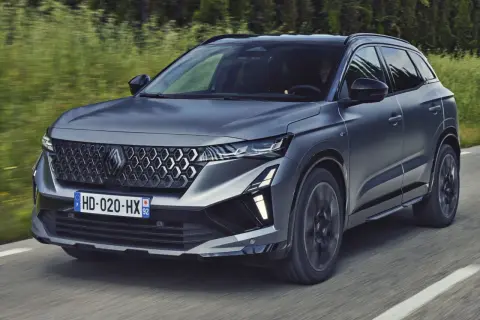 Nowy Renault Austral 2025 w ciemnoszarym kolorze pędzi po drodze, otoczony zielenią.