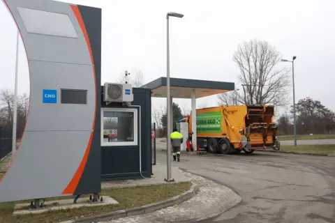 Stacja paliw z oznaczeniem CNG, gdzie można tankować gaz. Obok żółta śmieciarka z napisem "System Eko".