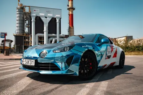 Błękitno-białe Alpine A110S z numerem 290 na tle przemysłowej zabudowy.