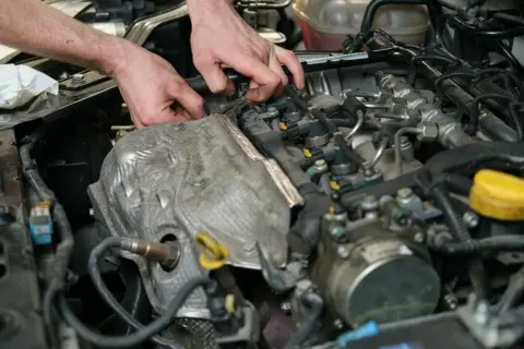 Mechanik pracuje przy silniku, wymieniając czujnik położenia wałka rozrządu.