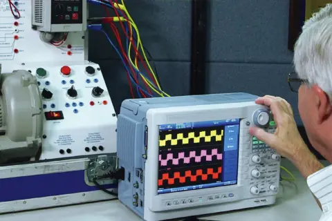 Mężczyzna reguluje oscyloskop, który pokazuje przebiegi, pomagając zrozumieć, jak zmierzyć moc silnika elektrycznego.