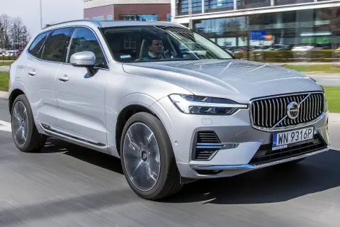 Srebrny Volvo XC60 T6 w ruchu miejskim, z kierowcą za kierownicą. Elegancki SUV na tle nowoczesnych budynków.