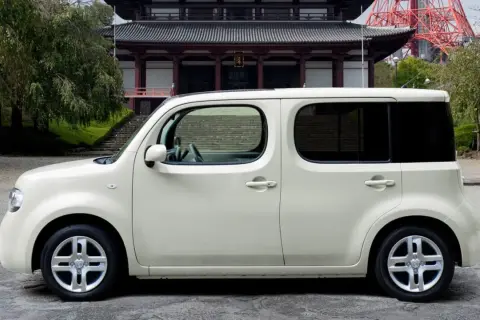 Biały Nissan Cube zaparkowany przed tradycyjną japońską świątynią.