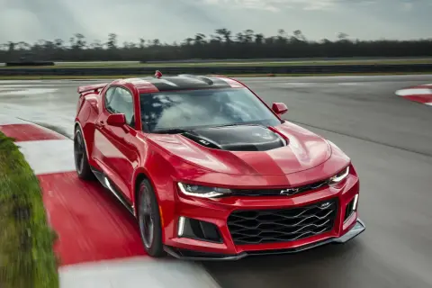 Czerwone Camaro ZL1 z czarnymi pasami pędzi po torze wyścigowym, zostawiając za sobą smugę prędkości.