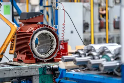 Część silnika elektrycznego z widocznym uzwojeniem, gotowa do montażu. W tle inne elementy produkcyjne, które mogą pomóc w zrozumieniu, jak obliczyć moc silnika elektrycznego.