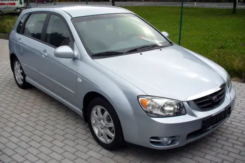 Jasnosrebrny Kia Cerato hatchback stoi na chodniku z kostki brukowej.