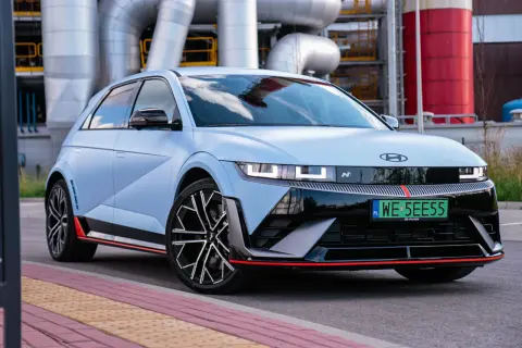 Niebieski Hyundai Ioniq 5 N z czerwonymi akcentami stoi przed przemysłowym budynkiem z rurami.