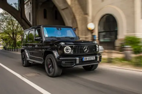 Czarny G-wagon pędzi pod wiaduktem, kierowca w okularach obserwuje drogę.