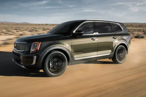 Ciemnozielony Kia Telluride przemierza pustynną drogę, unosząc kurz.