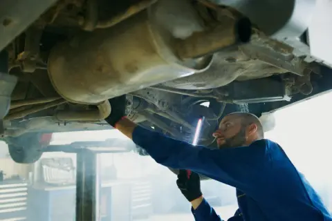 Mechanik w niebieskim kombinezonie oświetla latarką p0420 podwozie samochodu.