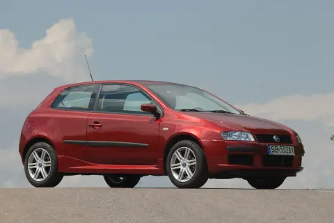 Czerwony Fiat Stilo 1.9 JTD z felgami aluminiowymi stoi na tle błękitnego nieba z chmurami.