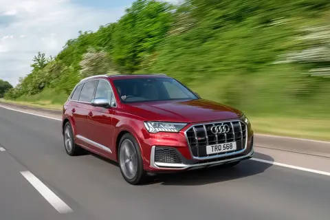 Czerwony Audi SQ7 pędzi po krętej drodze, otoczony zielenią.