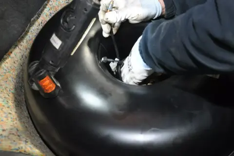 Ręce w rękawiczkach montują lub demontują okrągły zbiornik LPG w bagażniku samochodu.