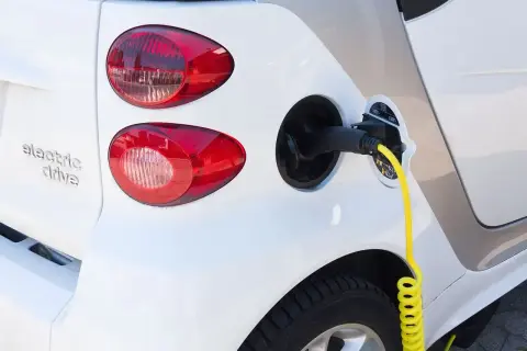 Biały samochód elektryczny z podłączonym żółtym kablem do ładowania.