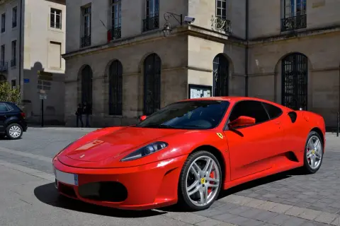 Czerwone Ferrari F430 zaparkowane na brukowanej ulicy przed kamienną budowlą.