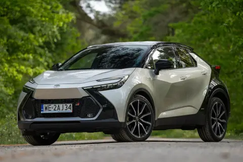 Nowy Toyota C-HR GR Sport w kolorze srebrnym z czarnym dachem, zaparkowany na leśnej drodze. Sprawdź atrakcyjną toyota chr cena!