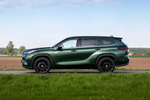 Zielony Toyota Grand Highlander z czarnymi felgami na tle pól i nieba.