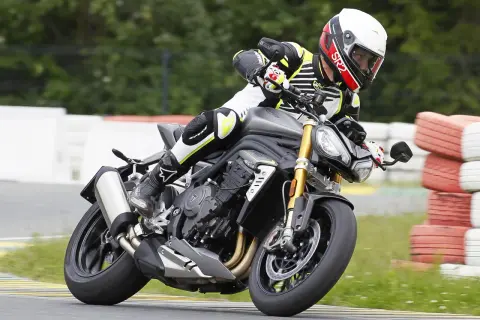 Motocyklista w kasku i kombinezonie pochyla się na torze wyścigowym na motocyklu Triumph Speed Triple.