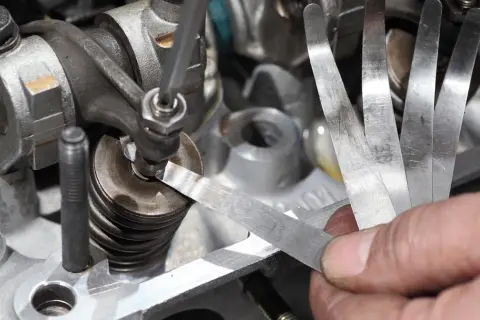 Mechanik sprawdza luzy zaworowe za pomocą szczelinomierza w silniku samochodowym.