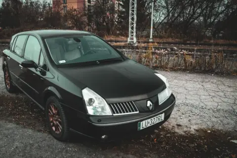 Czarny Renault Vel Satis z miedzianymi felgami stoi przy torach kolejowych.