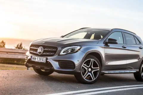 Szary Mercedes GLA 220 z polskimi tablicami rejestracyjnymi stoi na poboczu drogi o zachodzie słońca.