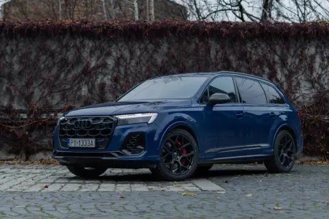 Elegancki, ciemnoniebieski Audi Q7 z czarnymi felgami i czerwonymi zaciskami hamulcowymi stoi na brukowanej nawierzchni.