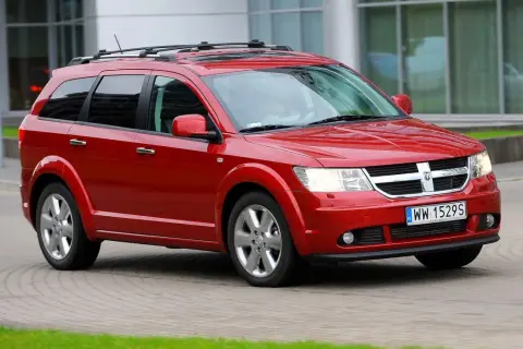 Czerwony Dodge Journey 3.6 z relingami dachowymi jedzie po brukowanej drodze.