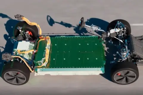 Podwozie samochodu elektrycznego z zieloną baterią i żółtymi kablami. Widoczne elementy układu napędowego i zawieszenia. Widać potencjalne natężenie pola elektrycznego wokół komponentów.