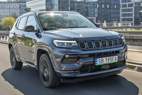 Ciemnoszary Jeep Compass 2025 na drodze, z nowoczesnymi budynkami w tle.