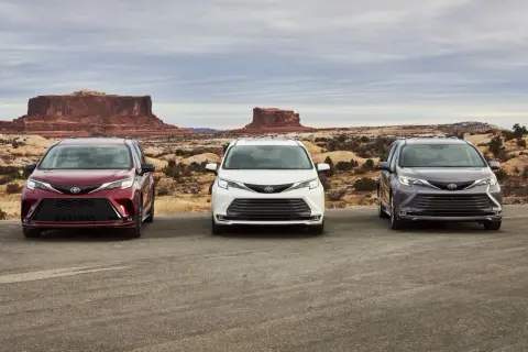 Trzy samochody Toyota Sienna w kolorach: wiśniowym, białym i grafitowym, stoją na tle pustynnego krajobrazu z formacjami skalnymi.