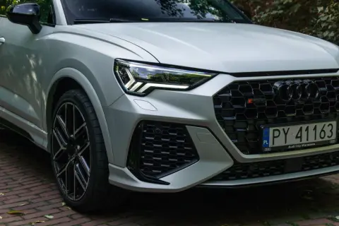 Srebrne Audi RS Q3 z czarnymi felgami i agresywnym grillem, gotowe do jazdy po warszawskich ulicach.