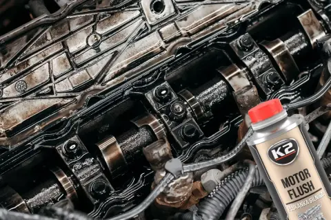 Zabrudzony silnik samochodowy i butelka K2 Motor Flush – dobra płukanka do silnika, która przywróci mu czystość i sprawność.