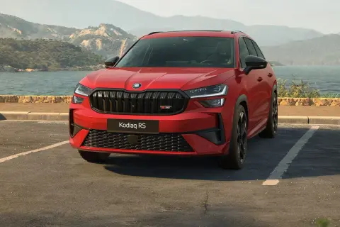 Czerwony Skoda Kodiaq RS zaparkowany nad jeziorem, z górami w tle.