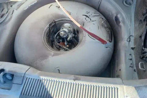 W bagażniku samochodu widać okrągłą butlę LPG, która wygląda na starą i zakurzoną. Czerwony przedmiot leży na jej powierzchni. Czas na wymianę, bo kończy się ważność butli LPG.