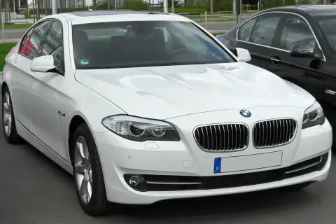 Białe BMW 535d z chromowanymi detalami i przyciemnianymi szybami, zaparkowane obok czarnego samochodu.