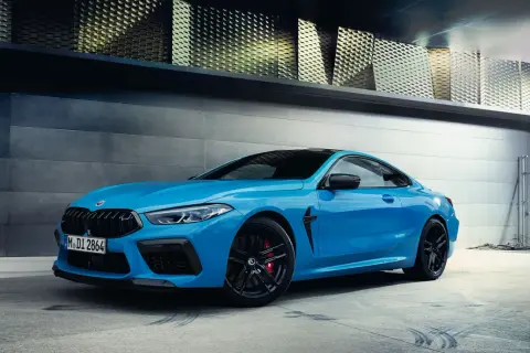 Niebieskie BMW M8 Coupe na tle nowoczesnej architektury.