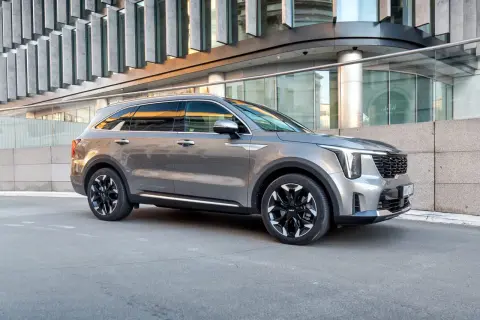 Elegancki, szary Kia Sorento 2025 z czarnymi felgami stoi przed nowoczesnym budynkiem.