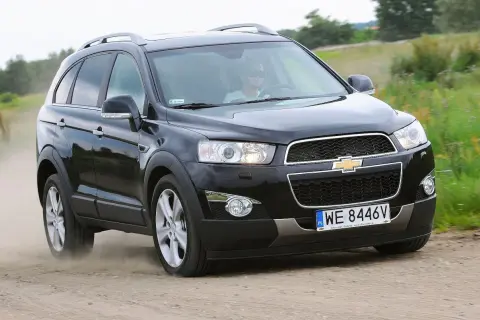 Czarny Chevrolet Captiva z kierowcą w okularach przeciwsłonecznych jedzie po piaszczystej drodze, wzbijając kurz.