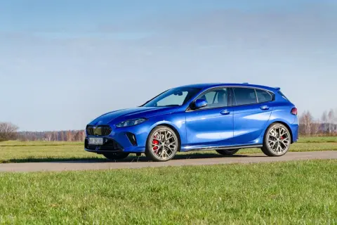 Błękitne BMW 120 na tle łąki i nieba. Sportowe felgi i czerwone zaciski hamulcowe dodają mu charakteru.