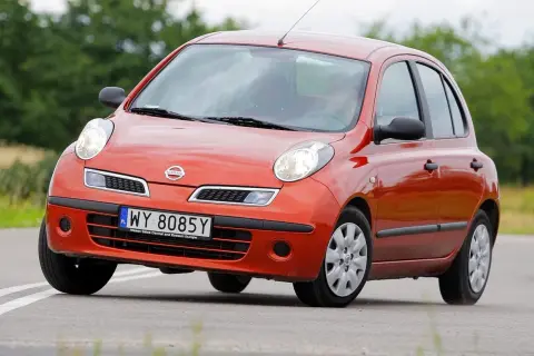 Pomarańczowy Nissan Micra K12 na drodze, z zielenią w tle.