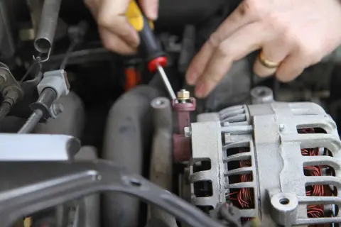Dłonie mechanika odkręcają śrubę przy alternatorze samochodu.