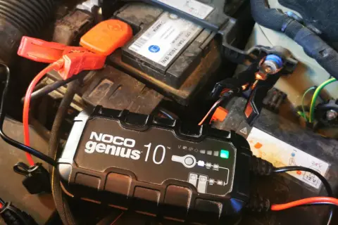 Ładowarka NOCO Genius 10 podłączona do akumulatora samochodowego, rozpoczyna proces odsiarczania akumulatora.