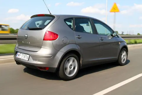 Szary Seat Altea XL jedzie po autostradzie. W tle widać żółty autobus i żółty znak ostrzegawczy.